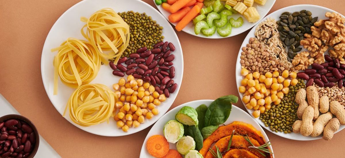A vibrant mix of legumes, vegetables, nuts, and pasta arranged on white plates showcasing a balanced, healthy diet.