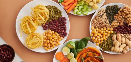 A vibrant mix of legumes, vegetables, nuts, and pasta arranged on white plates showcasing a balanced, healthy diet.